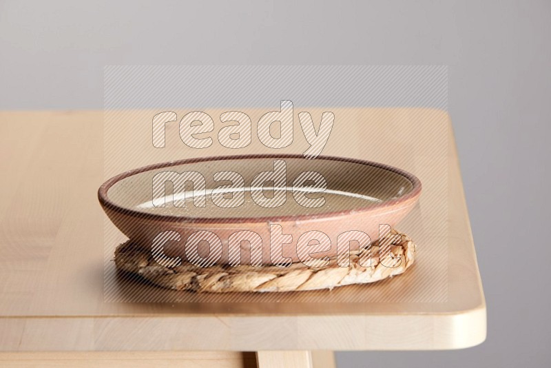 multi-colored pottery Plate placed on a small light colored straw placemat on the edge of wooden table