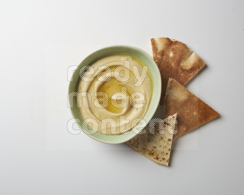 Hummus in a green plate garnished with olive oil on a white background