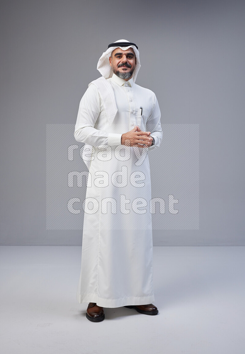 Saudi man Wearing Thob and white Shomag standing interacting with the camera on Gray background