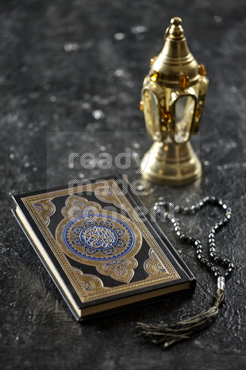 A golden lantern with different drinks, dates, nuts, prayer beads and quran on textured black background