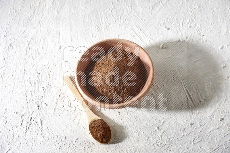 A wooden bowl and a wooden spoon full of cloves powder on a textured white flooring