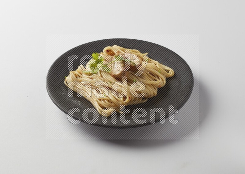 spaghetti pasta with white sauce on a black plate on a white background