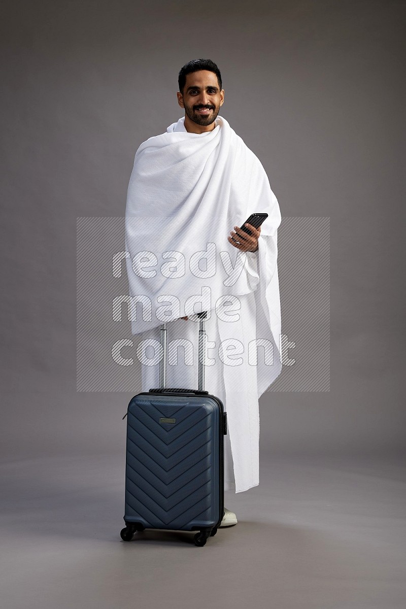 A man wearing Ehram Standing holding traveling bag on gray background