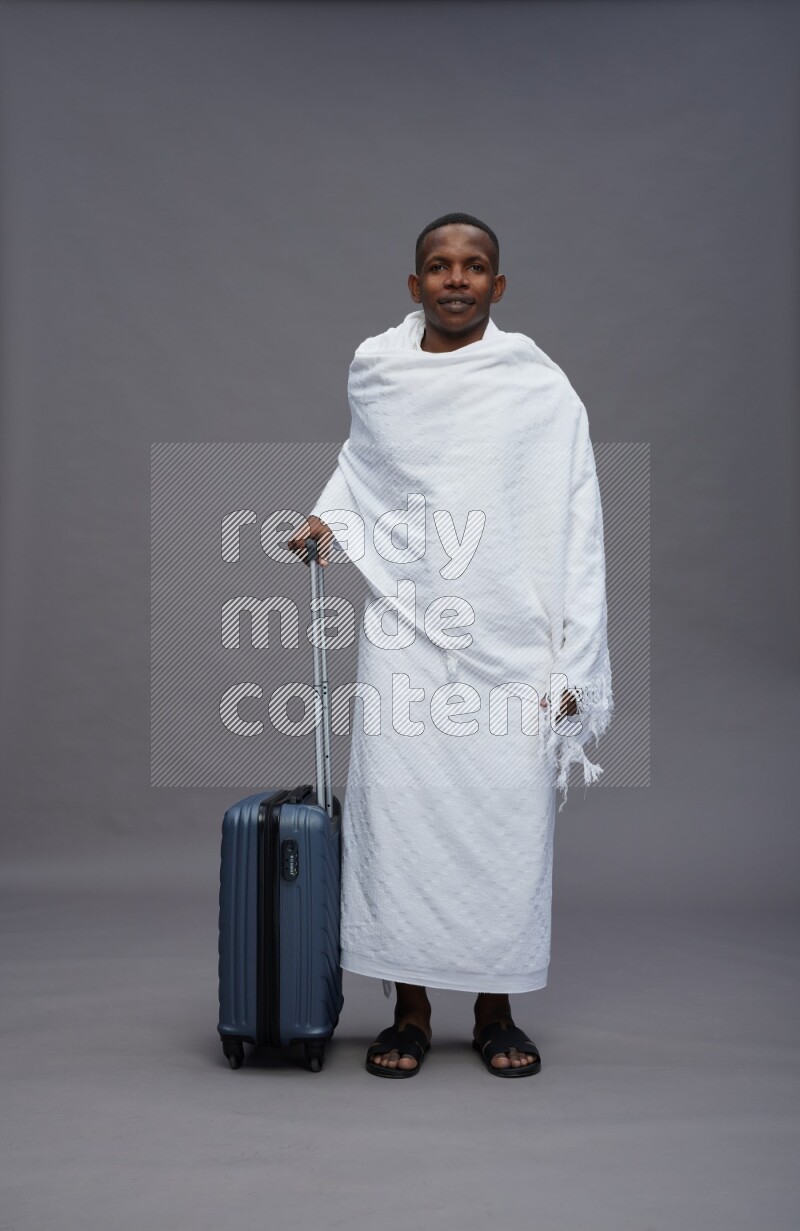 A man wearing Ehram Standing holding traveling bag on gray background