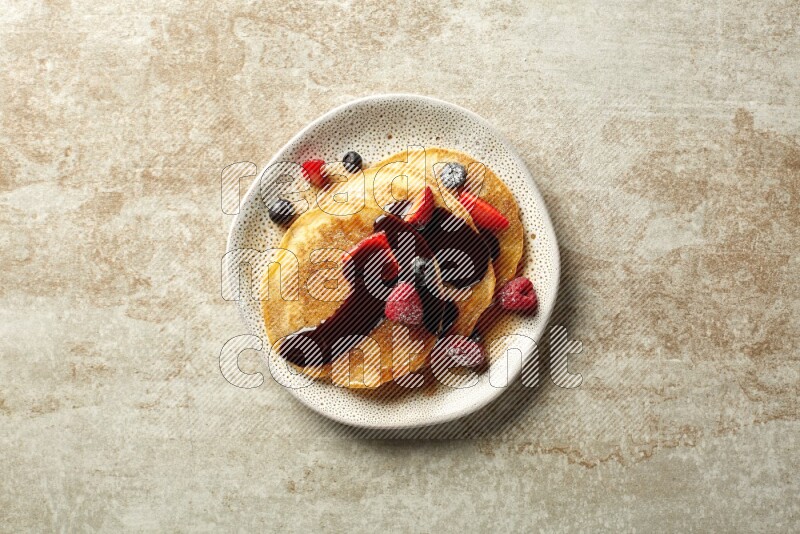 Three stacked mixed berries pancakes in an irregular plate on beige background