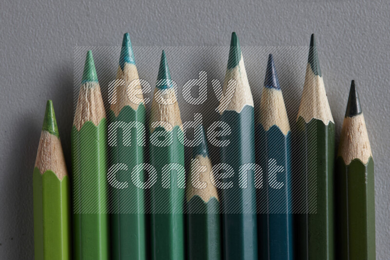 مجموعة من أقلام الرصاص الملونة مرتبة لتعرض تدرجا من الألوان الخضراء علي خلفية رمادية