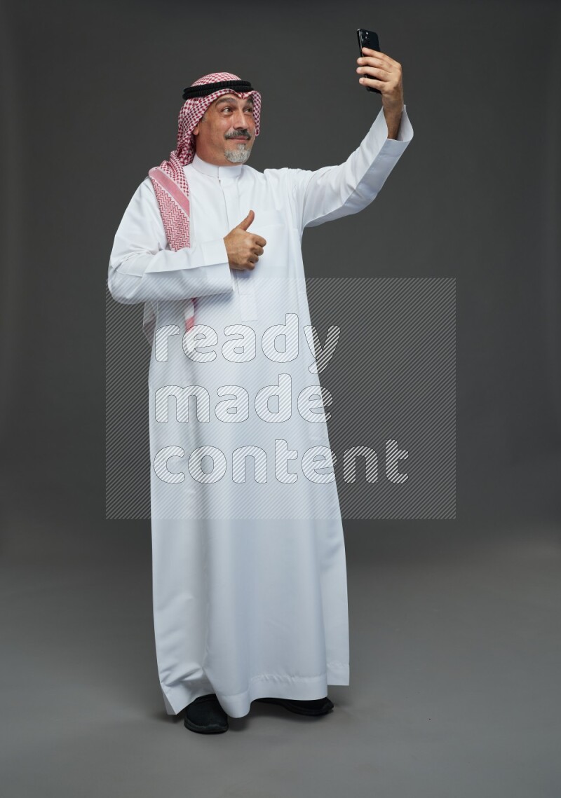 Saudi man with shomag Standing taking selfie on gray background