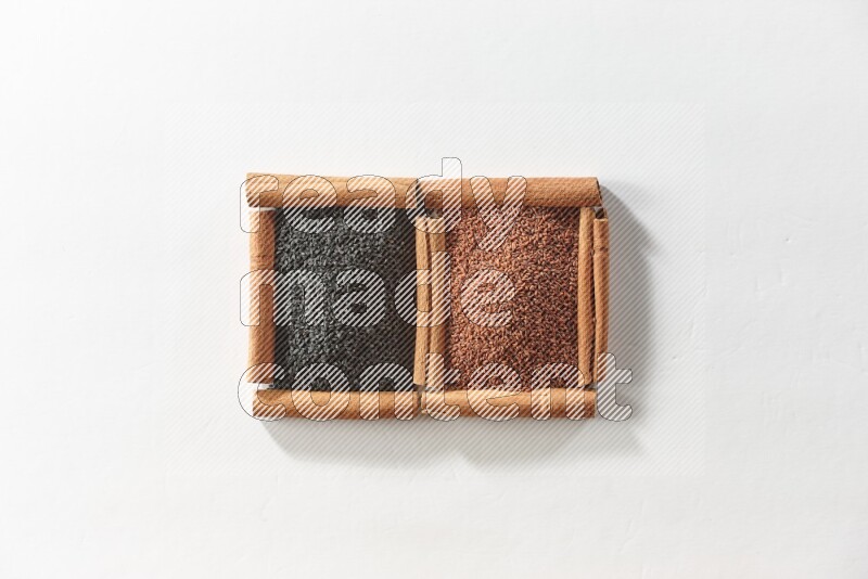 مربعان من أعواد القرفة ممتلئان بحبة البركة السوداء وبذور الكتان علي خلفية بيضاء