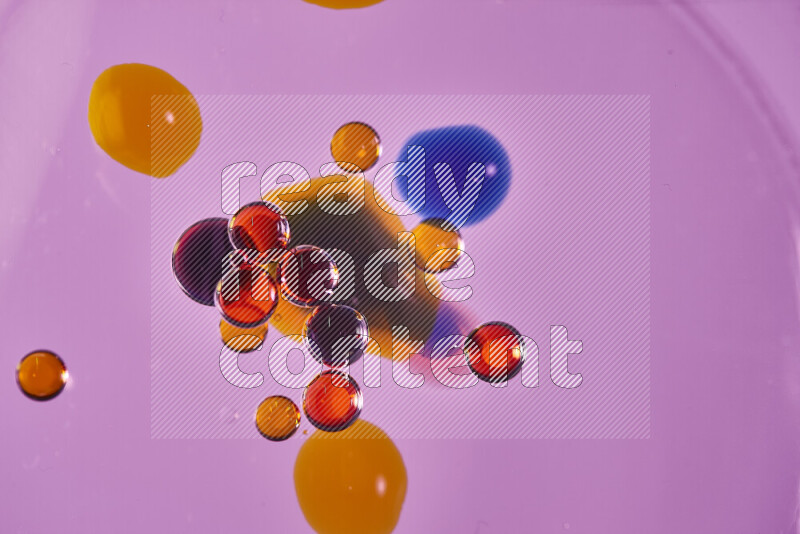 Close-ups of abstract red, blue and yellow watercolor drops on oil Surface on pink background