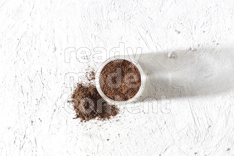 A glass jar full of cloves powder on a textured white flooring