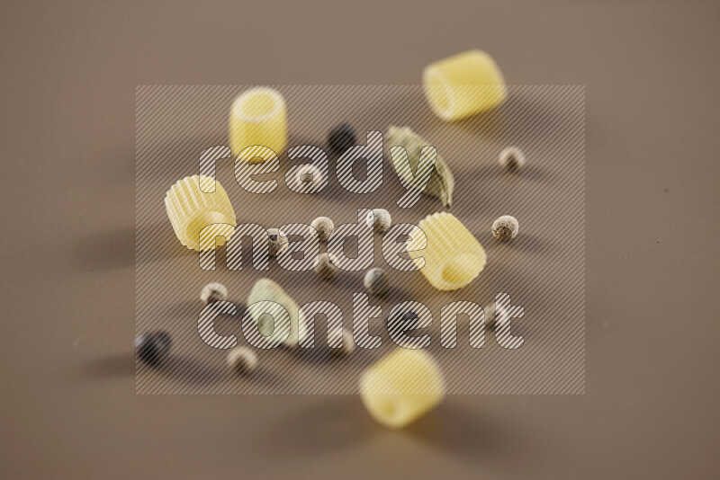 Raw pasta with different ingredients such as cherry tomatoes, garlic, onions, red chilis, black pepper, white pepper, bay laurel leaves, rosemary and cardamom on beige background