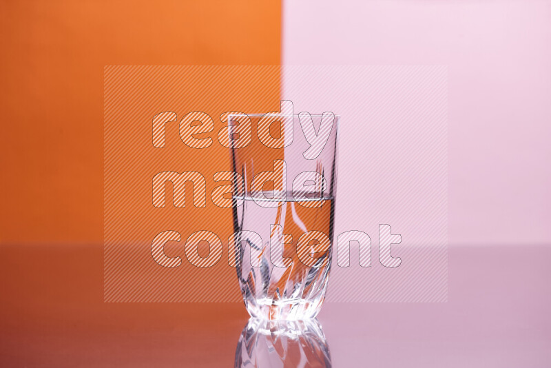 The image features a clear glassware filled with water, set against orange and rose background