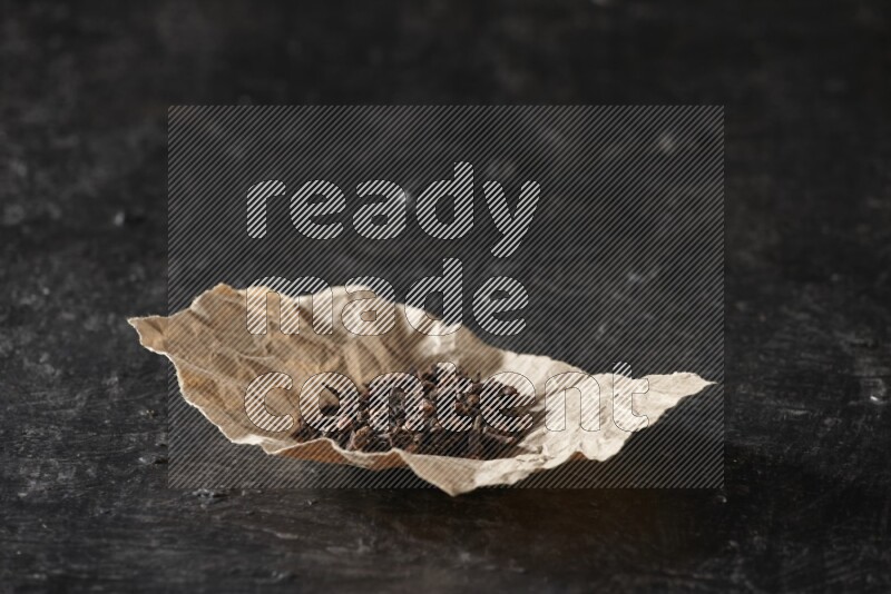 Cloves in crumpled piece of paper on a textured black flooring