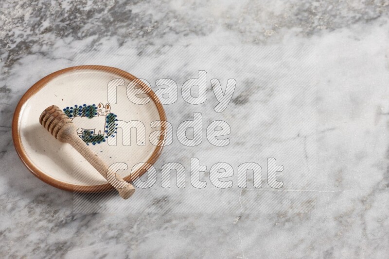 Decorative pottery plate with wooden honey dipper in it on grey marble background