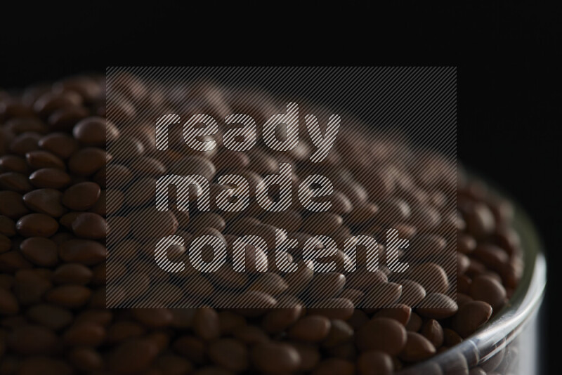 Brown lentils in a glass jar on black background