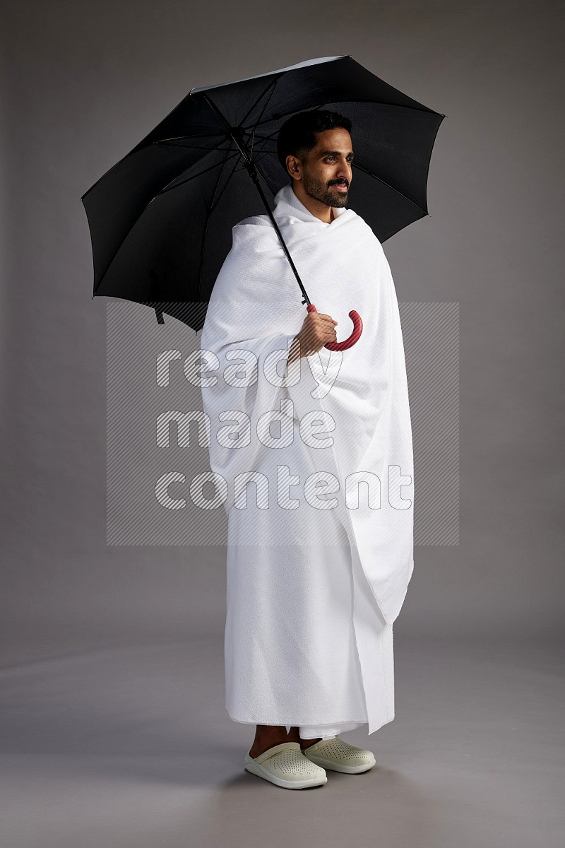 A man wearing Ehram Standing holding umbrella on gray background