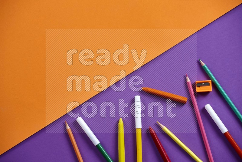 A mix of colored pencils, pens, crayons on orange and purple background (kids toys)