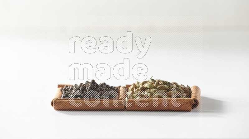 مربعان من أعواد القرفة ممتلئان بحبوب الهيل وحبوب الفلفل الأسود علي خلفية بيضاء