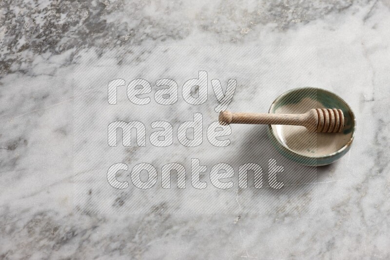 Multicolored pottery bowl with wooden honey dipper in it on grey marble background