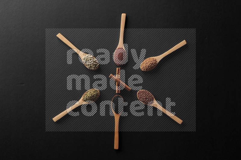 wooden spoons filled with white peppers, mustard seeds, black seeds, garden cress, cumin and flax on black flooring and shaped like a clock