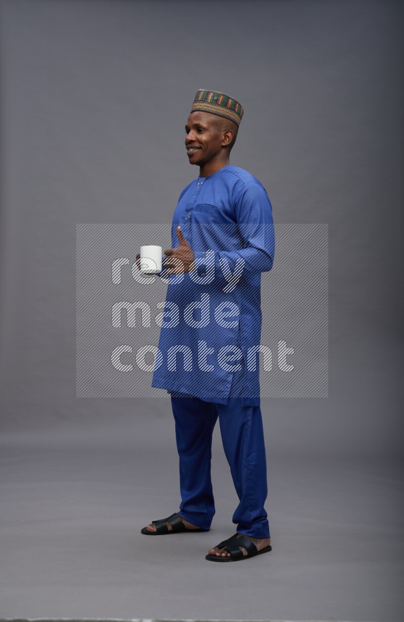 Man wearing Nigerian outfit standing holding mug on gray background