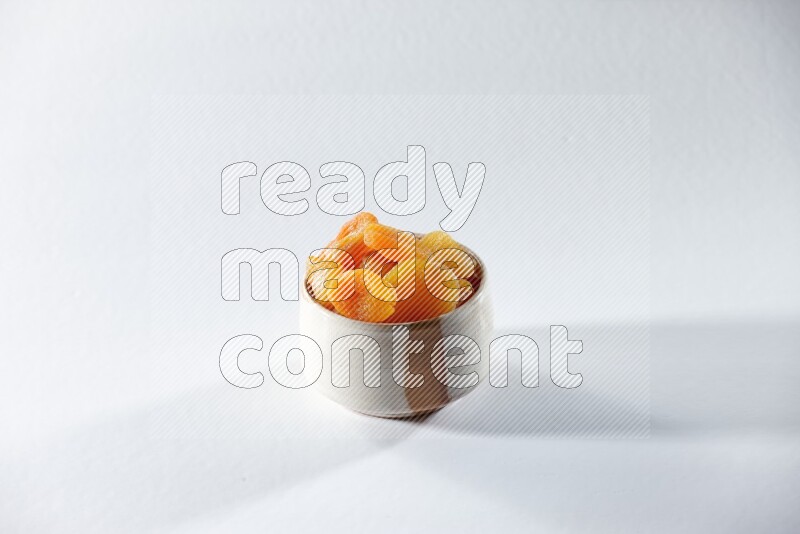 A beige ceramic bowl full of dried apricots on a white background in different angles