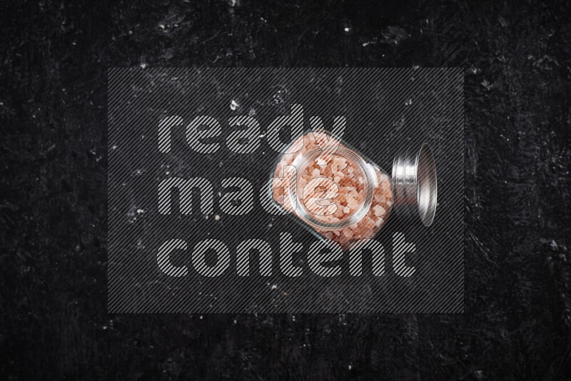A glass jar full of coarse himalayan salt crystals on black background