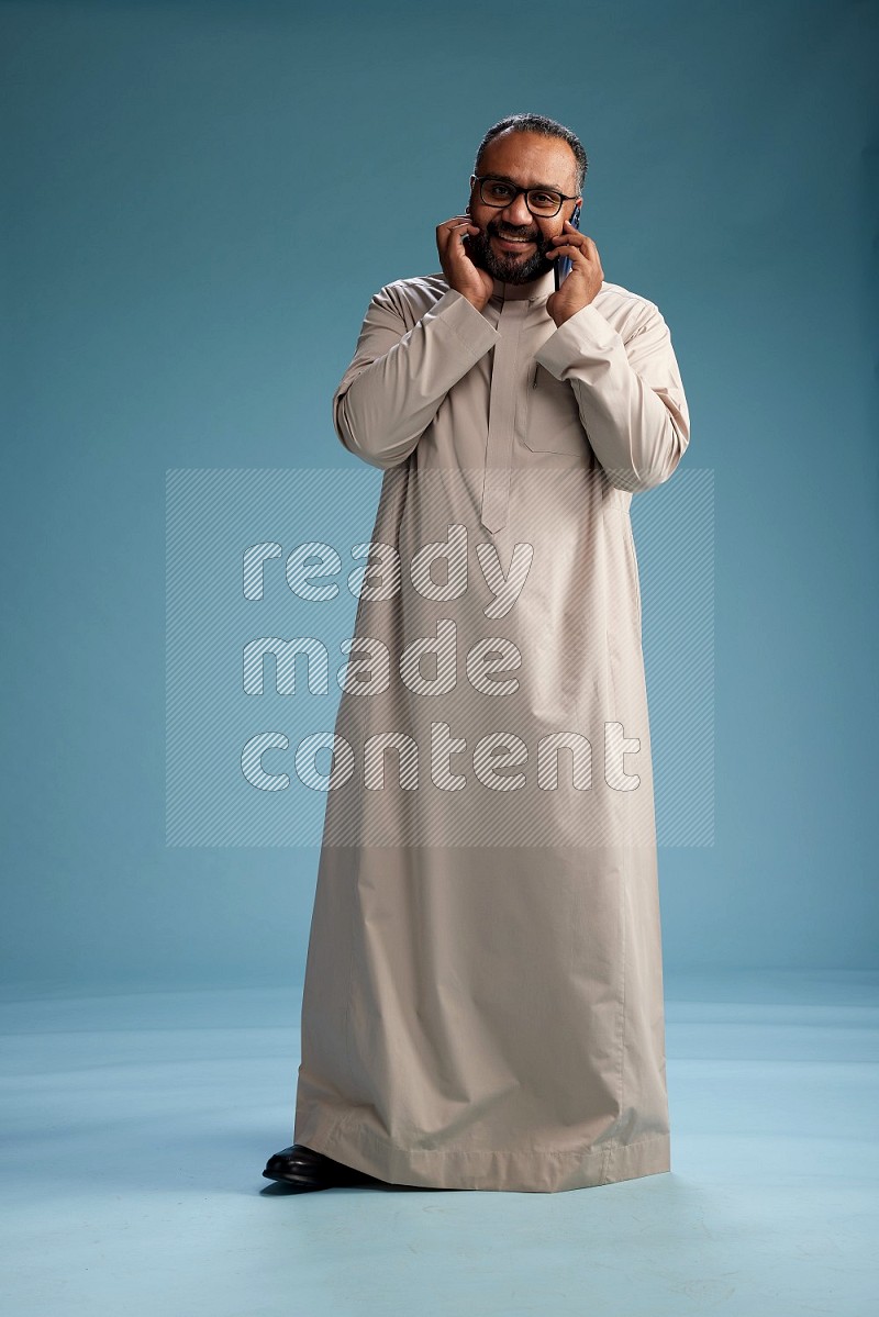 Saudi Man without shimag Standing talking on phone on blue background