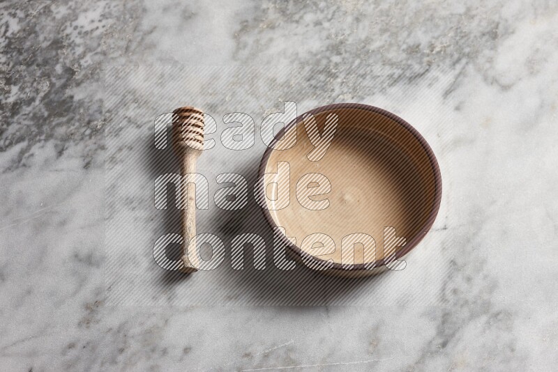 Beige pottery oven bowl with wooden honey dipper on the side on grey marble background