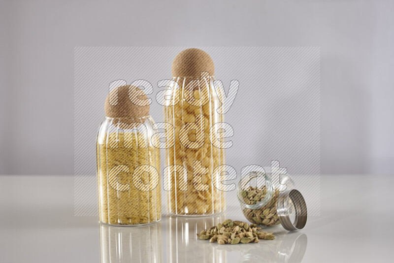 Raw pasta in glass jars with cardamom on light grey background