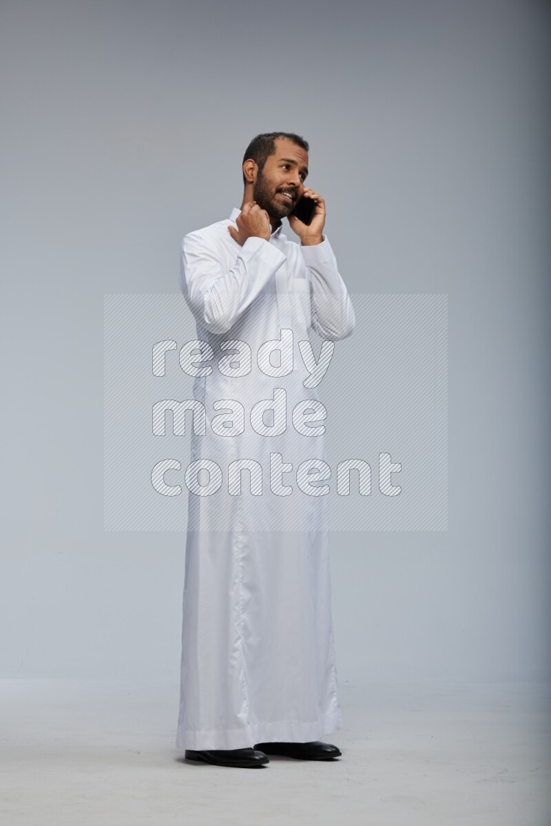 Saudi man wearing Thob standing talking on phone on Gray background