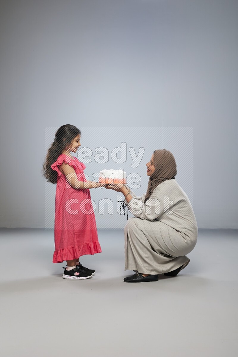 A mother giving a cake to her daughter on gray background