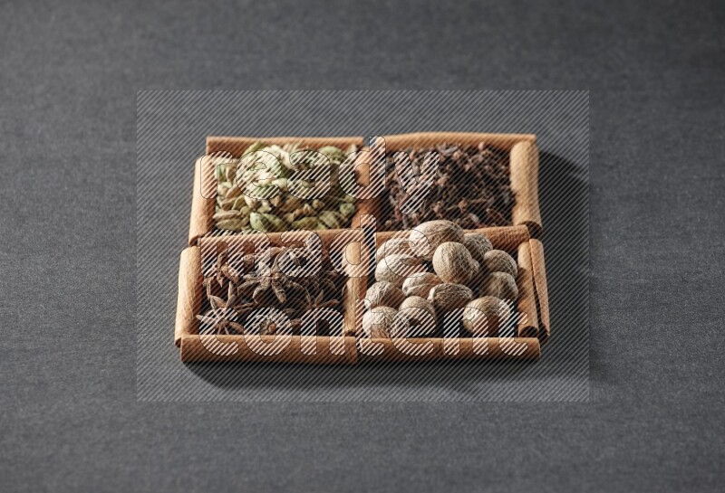 4 مربعات من عيدان القرفة ممتلئة بحب الهيل واليانسون النجمي وجوزة الطيب والقرنفل على أرضية سوداء