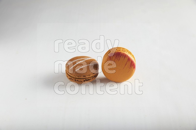 45º Shot of of two assorted Brown Irish Cream, and Orange Exotic macarons on white background