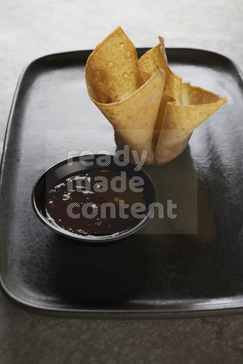 wonton cups with soy sauce ramkin on rectangle dark grey ceramic plate on grey textured counter top