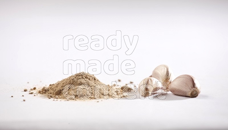 A small pile of garlic powder with some of cloves and a whole garlic bulb on a white flooring