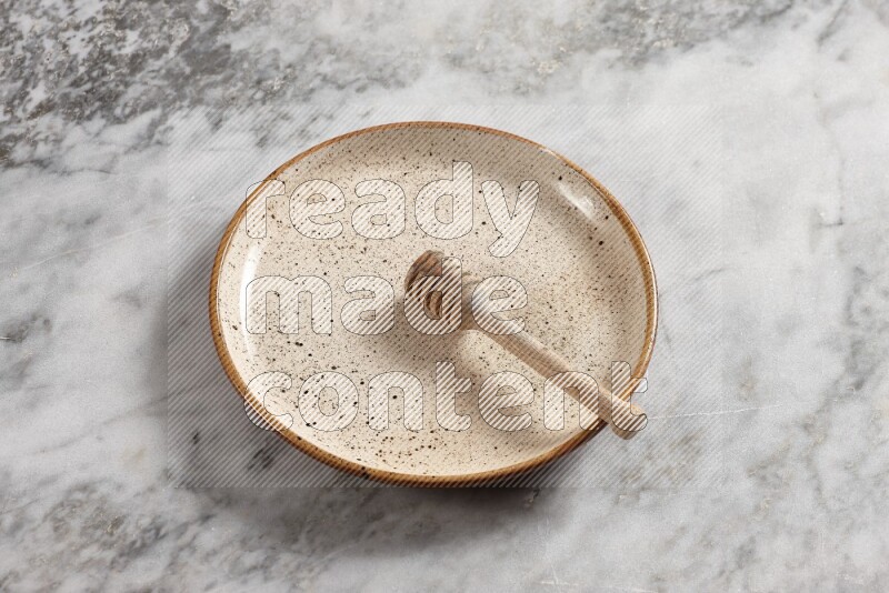 Beige pottery plate with wooden honey dipper in it on grey marble background