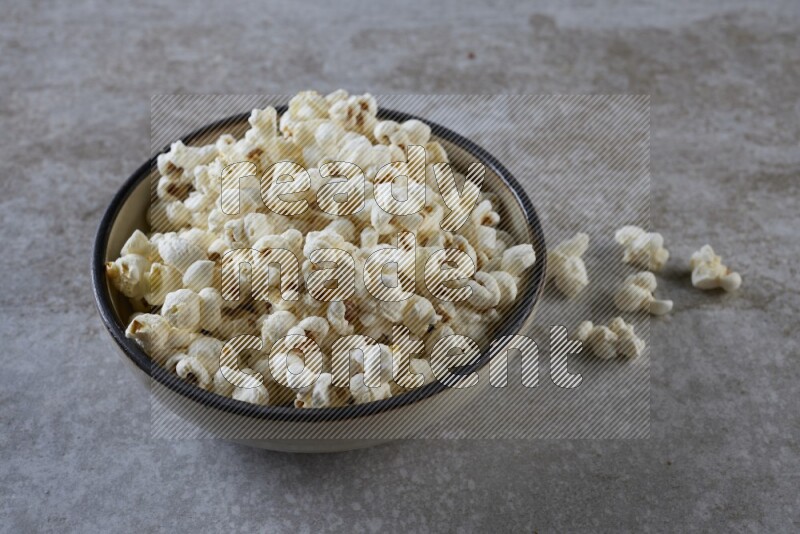 popcorn in a multi-colored pottery bowl on a grey textured countertop