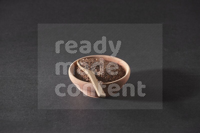 وعاء خشبي ممتلئ بحبوب بذر الكتان مع ملعقة خشبية ممتلئة بالحبوب علي خلفية سوداء