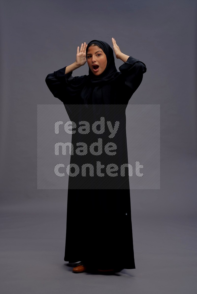 Saudi woman wearing Abaya standing hands behind head on gray background