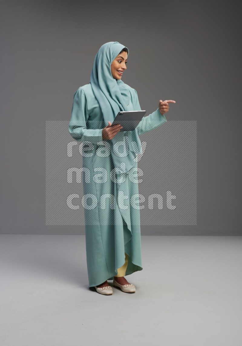 Saudi Woman wearing Abaya standing working on tablet on Gray background