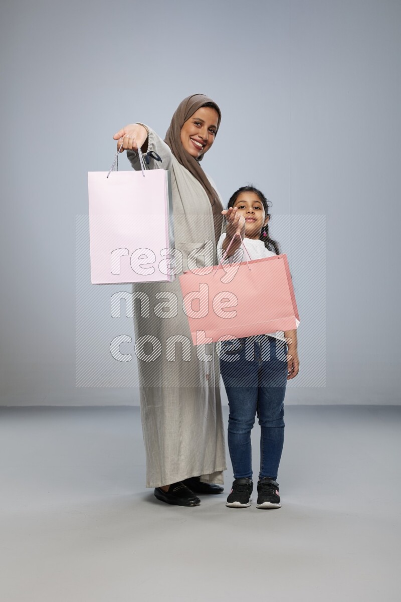 Mom and daughter holding shopping bags on gray background