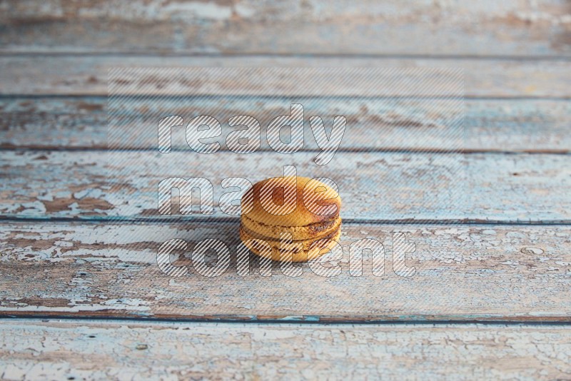 45º Shot of Yellow Crème Brulée macaron on light blue wooden background