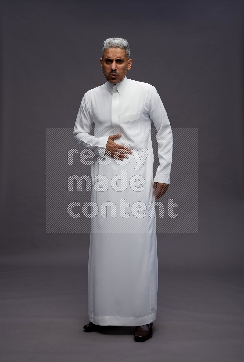 Saudi man wearing thob standing interacting with the camera on gray background