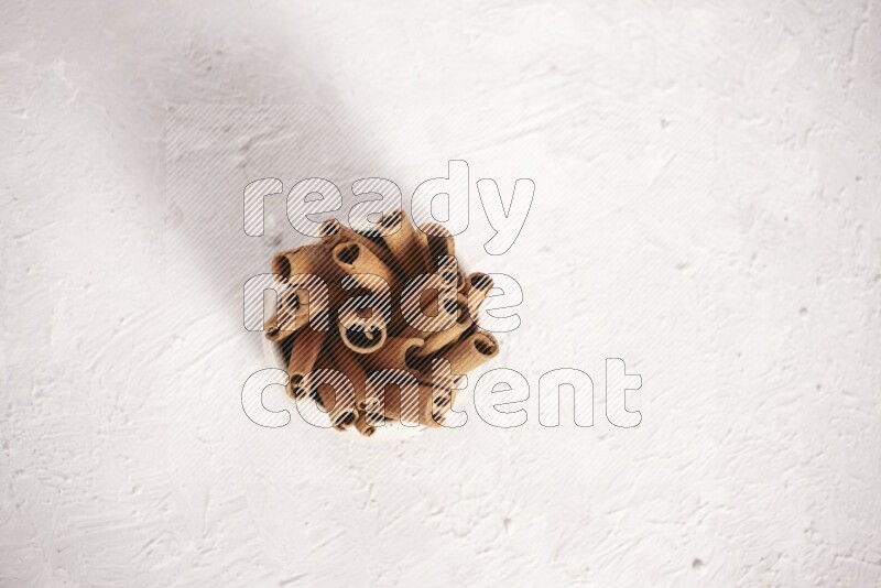 Cinnamon sticks in a beige bowl on a white background