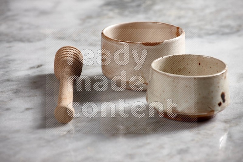 Multicolored Pottery bowls with wooden honey handle on the side with grey marble flooring, 15 degree angle