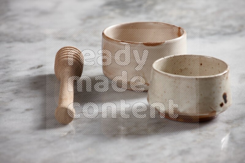 Multicolored pottery bowls with wooden honey dipper on the side on grey marble background