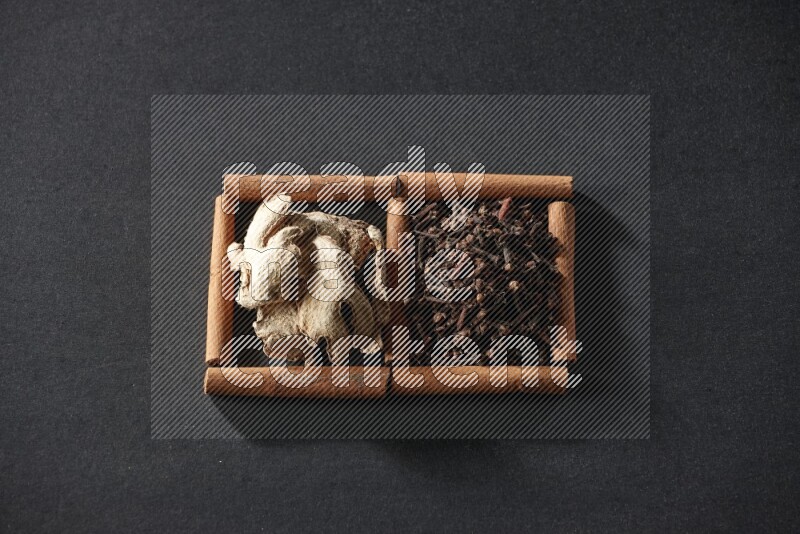 2 squares of cinnamon sticks full of cloves and dried ginger on black flooring