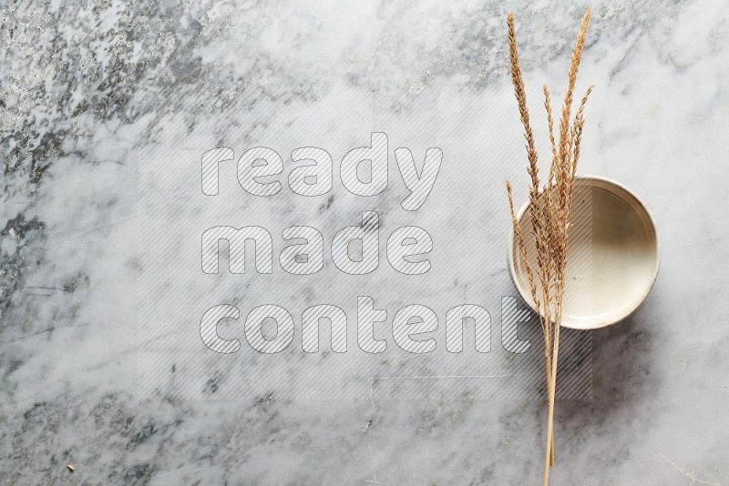 Wheat stalks on Beige Pottery Bowl on grey marble flooring, Top view