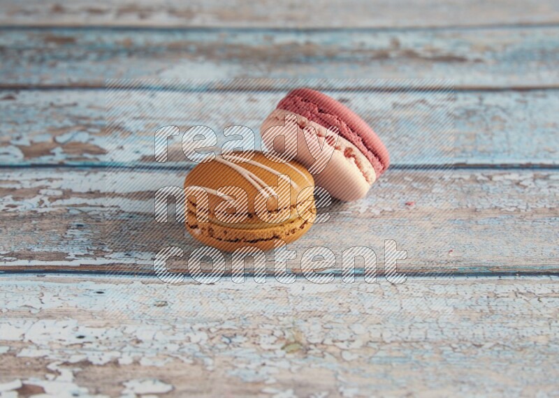 45º Shot of of two assorted Brown Irish Cream, and Pink Litchi Raspberry macarons on light blue background